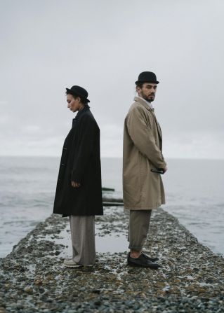 Couple standing back-to-back on a rocky pier by the sea, evoking themes of isolation and contemplation.