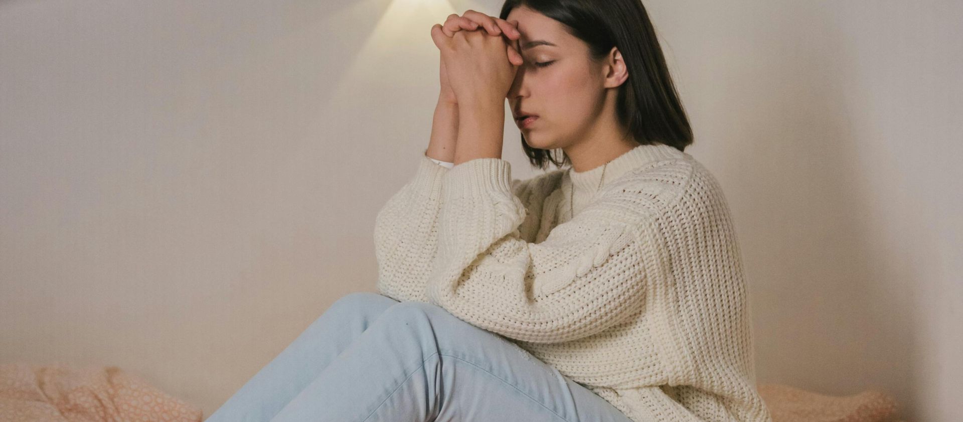 Woman in a cozy bedroom, wearing comfort clothes, meditating with eyes closed.